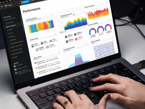 Hands typing on a laptop keyboard displaying the Aviat Networks radio router performance dashboard UI with metrics for usage, temperature, frequency spectrum, and system alarms.