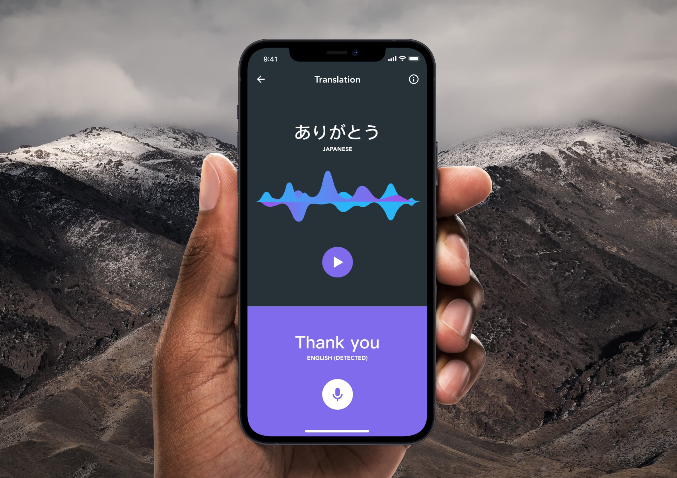 Hand holding an iPhone showing a voice translation app interface against a mountain background.