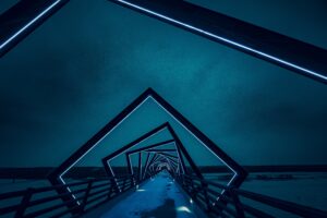 Night perspective looking through the glowing blue geometric steel arches of the High Trestle Trail Bridge, showcasing modern architectural lighting and linear perspective.