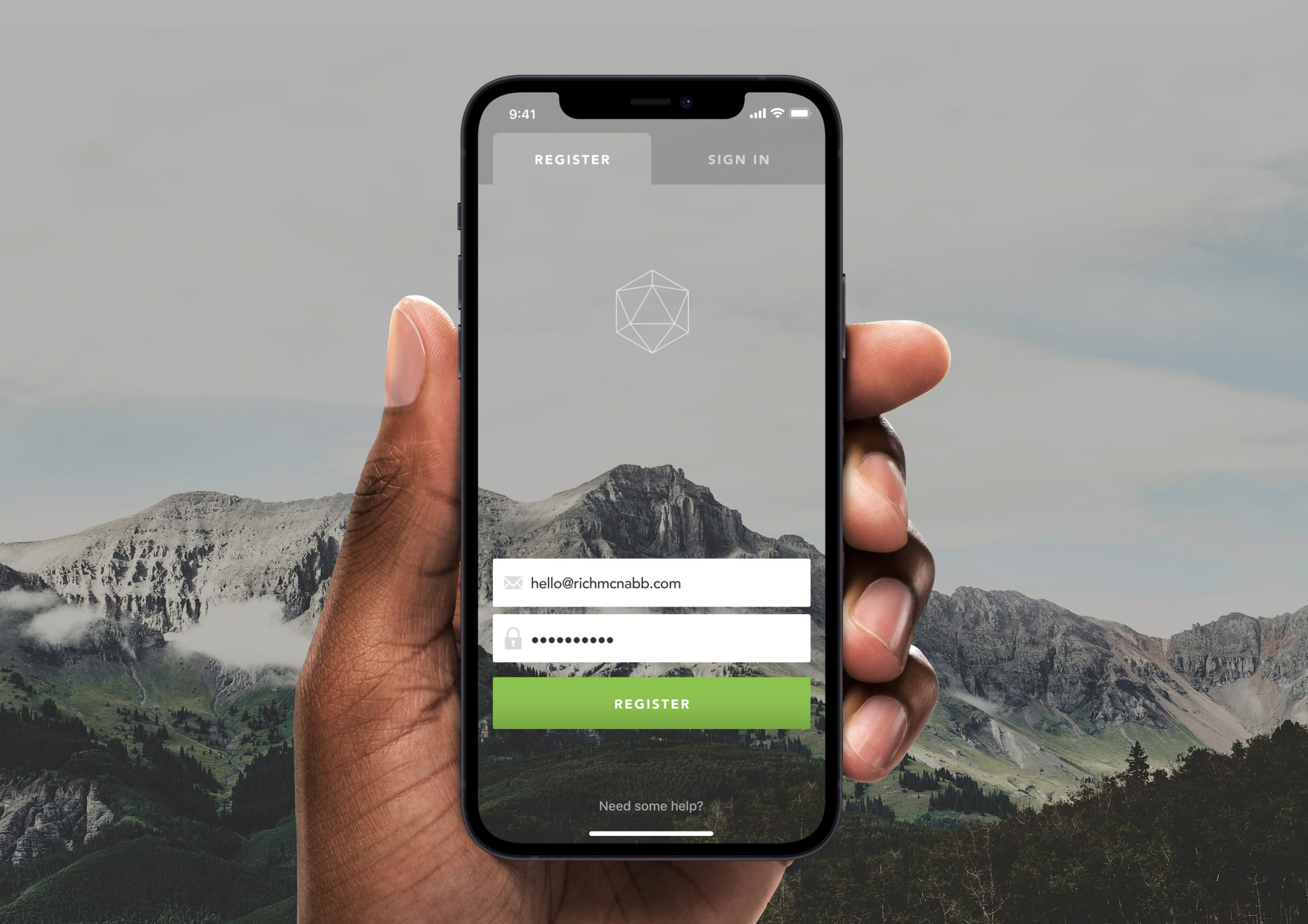 Hand holding a black iPhone displaying a registration screen set over a foggy mountain landscape background.
