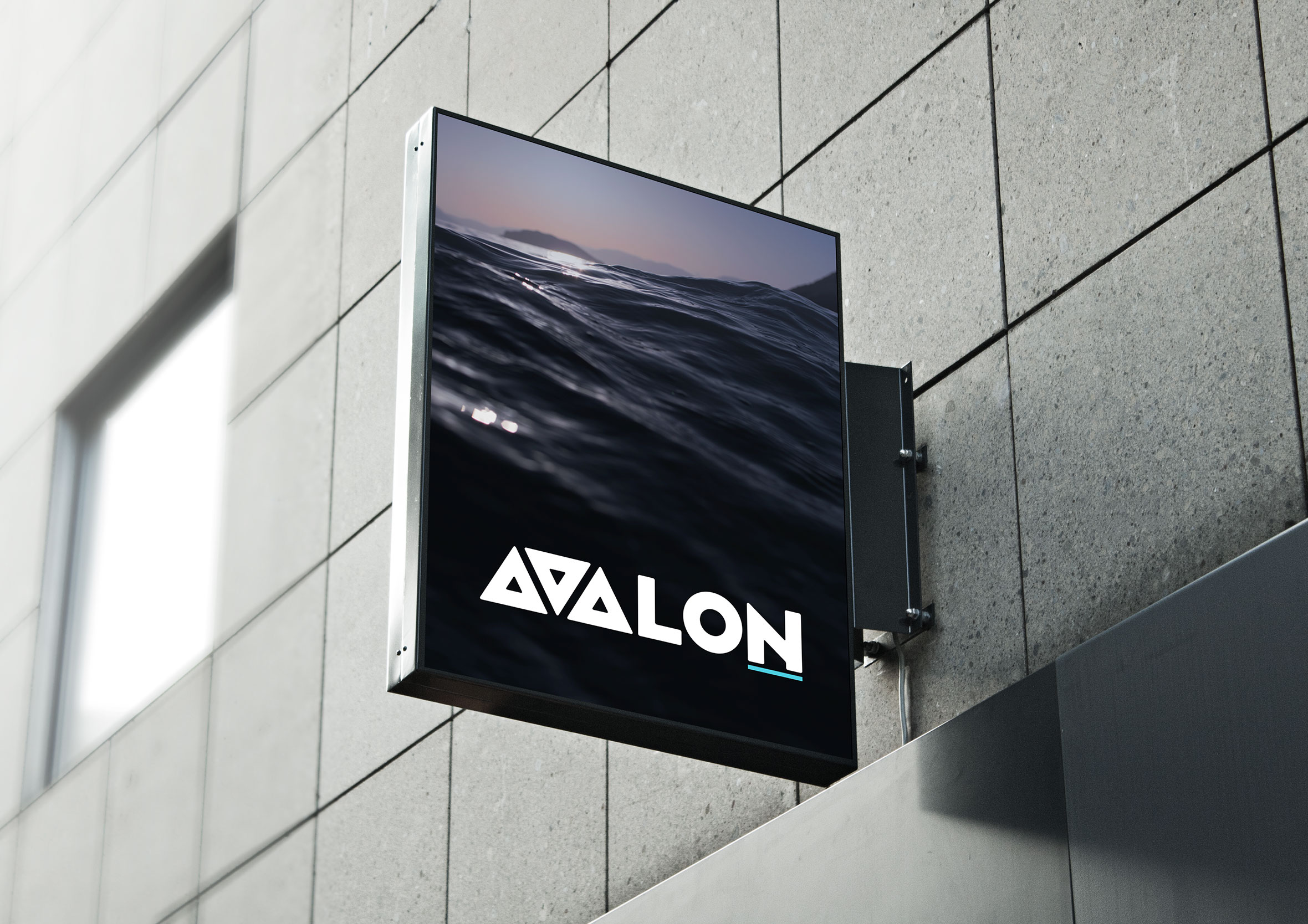 Square black exterior blade sign featuring the Avalon logo mounted on a grey tiled building facade.
