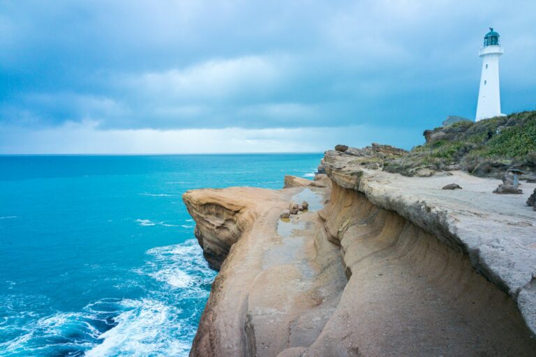 Scenic view of Castlepoint Lighthouse towering over rugged sandstone cliffs above bright blue ocean waters, capturing coastal landscapes and New Zealand landmarks.