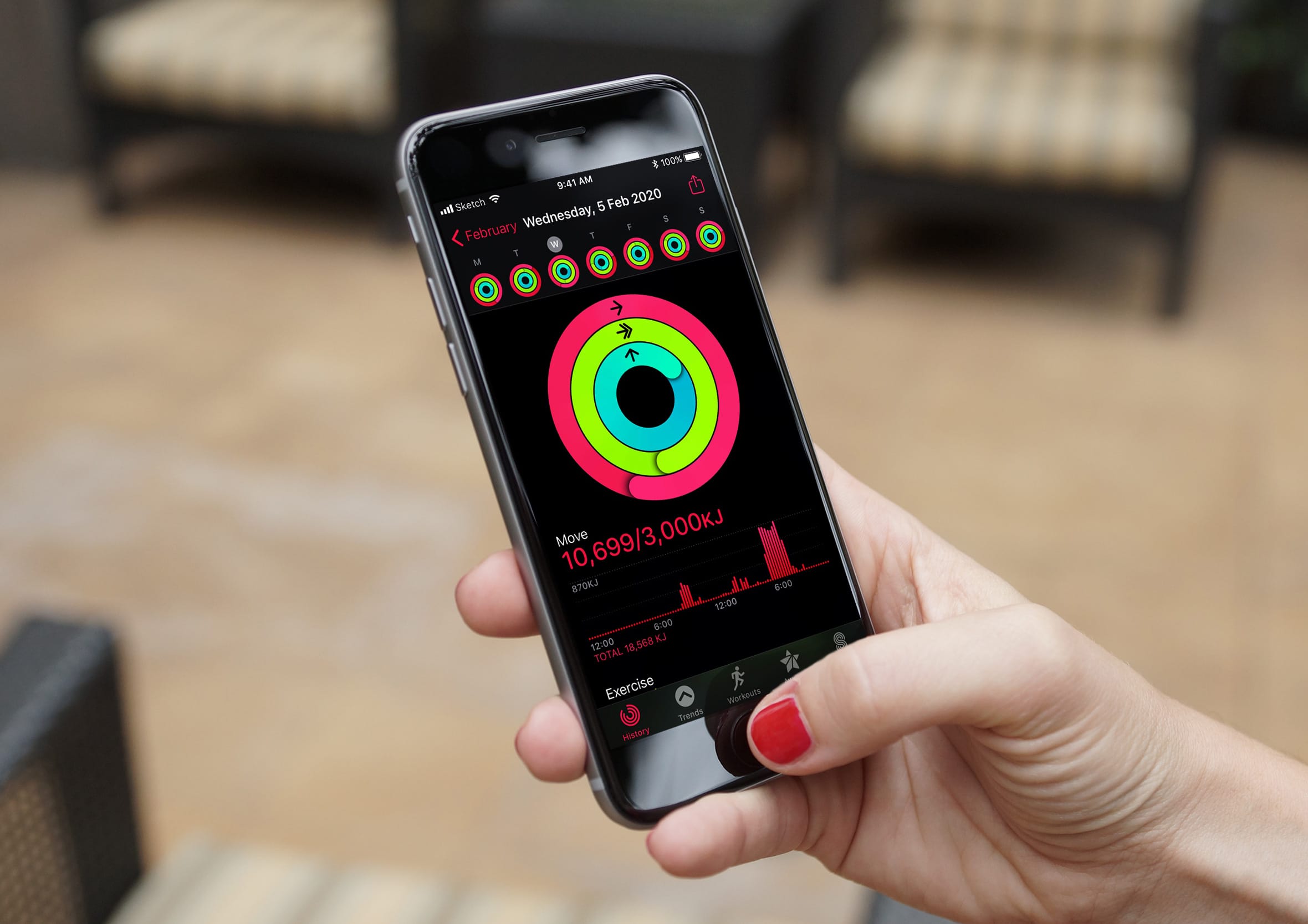 Hand holding an iPhone displaying the Apple Watch Activity app interface showing completed fitness rings, daily kilojoule counts, and workout history charts for tracking health goals.