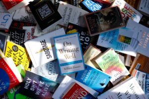 Flat-lay composition of non-fiction books including On Writing Well and Outliers spread across a table, reflecting continuous learning and research habits.