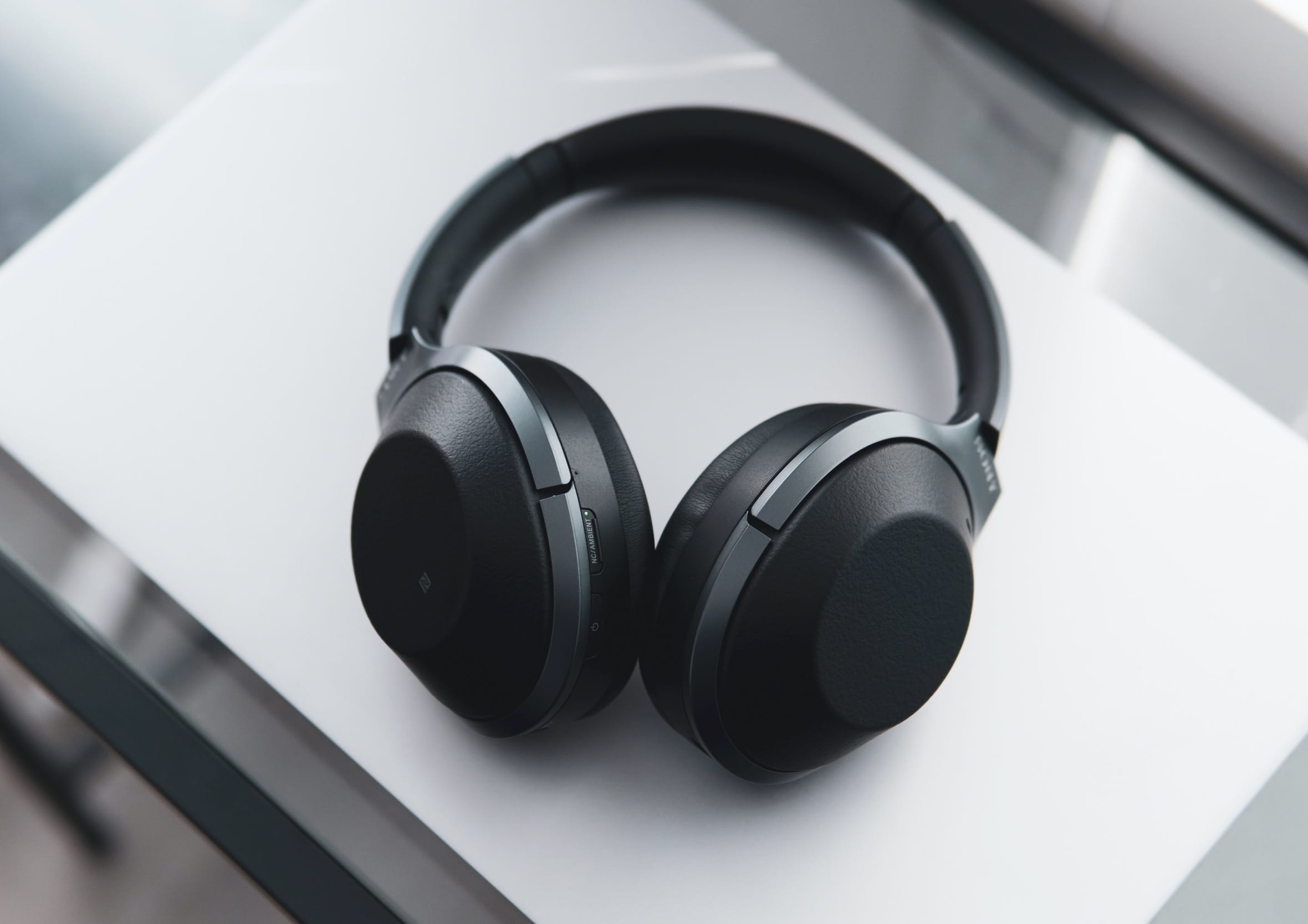 Black Sony over-ear noise-cancelling headphones resting on a light desk surface featuring tactile physical control buttons and matte finish for focused audio listening.