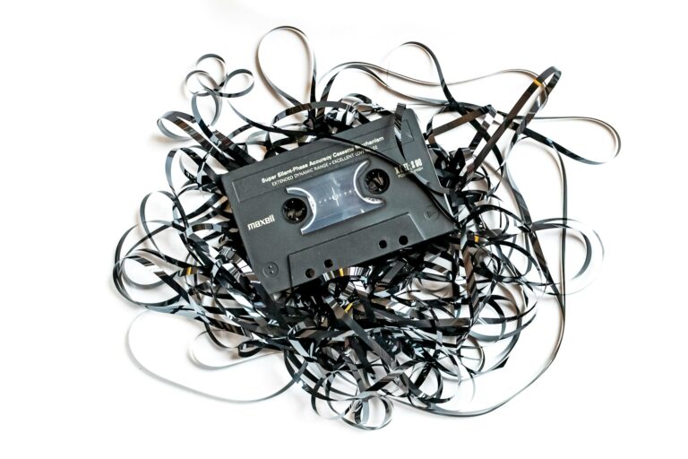 Black cassette tape lying on a white background surrounded by a tangled heap of unspooled magnetic tape, representing analogue media and audio preservation.