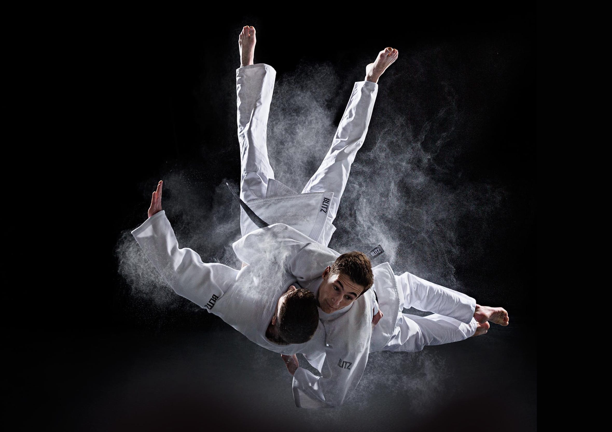 Two TKD martial artists wearing white gi executing a dramatic mid-air throw with chalk dust effects