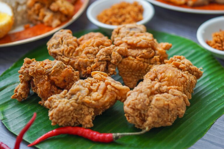 Golden baked chicken pieces served on a fresh green banana leaf with a red chilli garnish, capturing culinary styling and food photography.