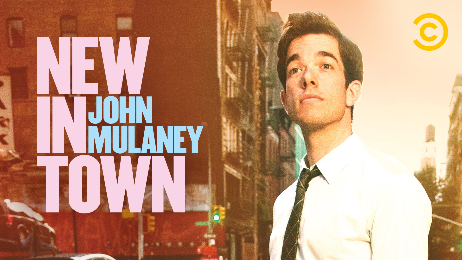 Promo card for John Mulaney's stand-up comedy special New in Town showing Mulaney in a dark suit and tie.
