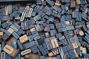 Overhead view of a pile of varied wooden and metal letterpress type blocks, reflecting tactile typography and print production heritage.