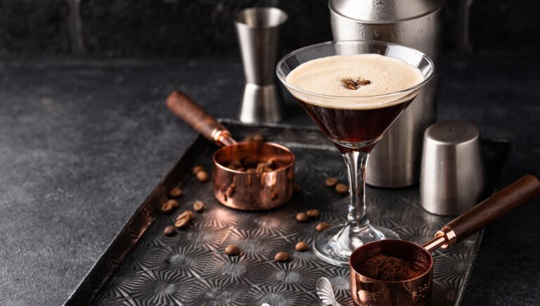 Espresso martini cocktail topped with coffee beans in a martini glass next to copper measuring scoops, highlighting hospitality presentation and craft beverage detail.