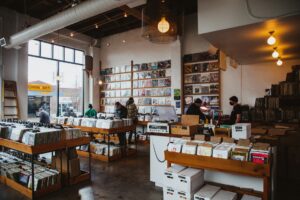 Wide shot of customers browsing wooden record bins inside a sunlit vinyl shop, showcasing physical music discovery and retail environment design.