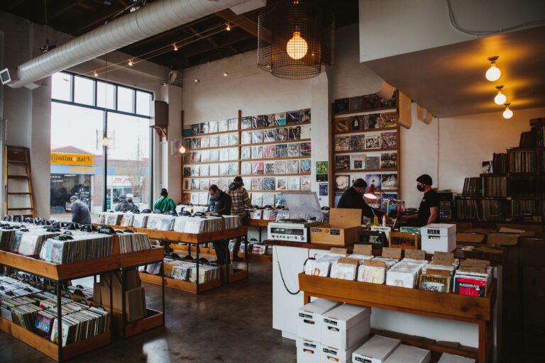 Wide shot of customers browsing wooden record bins inside a sunlit vinyl shop, showcasing physical music discovery and retail environment design.