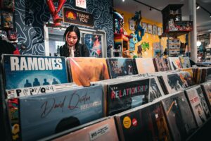 Young woman browsing through rows of classic vinyl record sleeves inside a brightly lit vintage music shop, reflecting tactile user discovery and media curation.