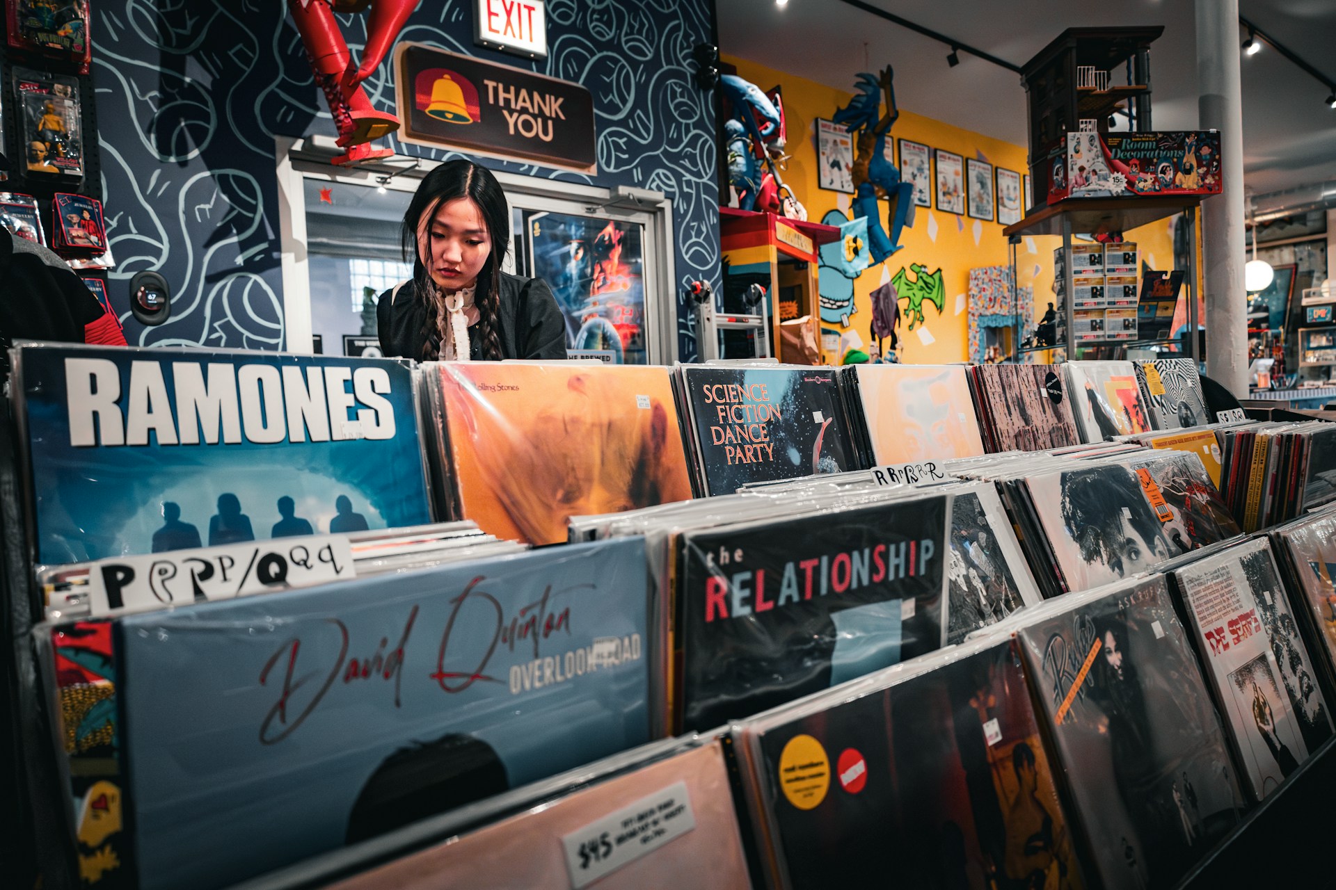 Young woman browsing through rows of classic vinyl record sleeves inside a brightly lit vintage music shop, reflecting tactile user discovery and media curation.