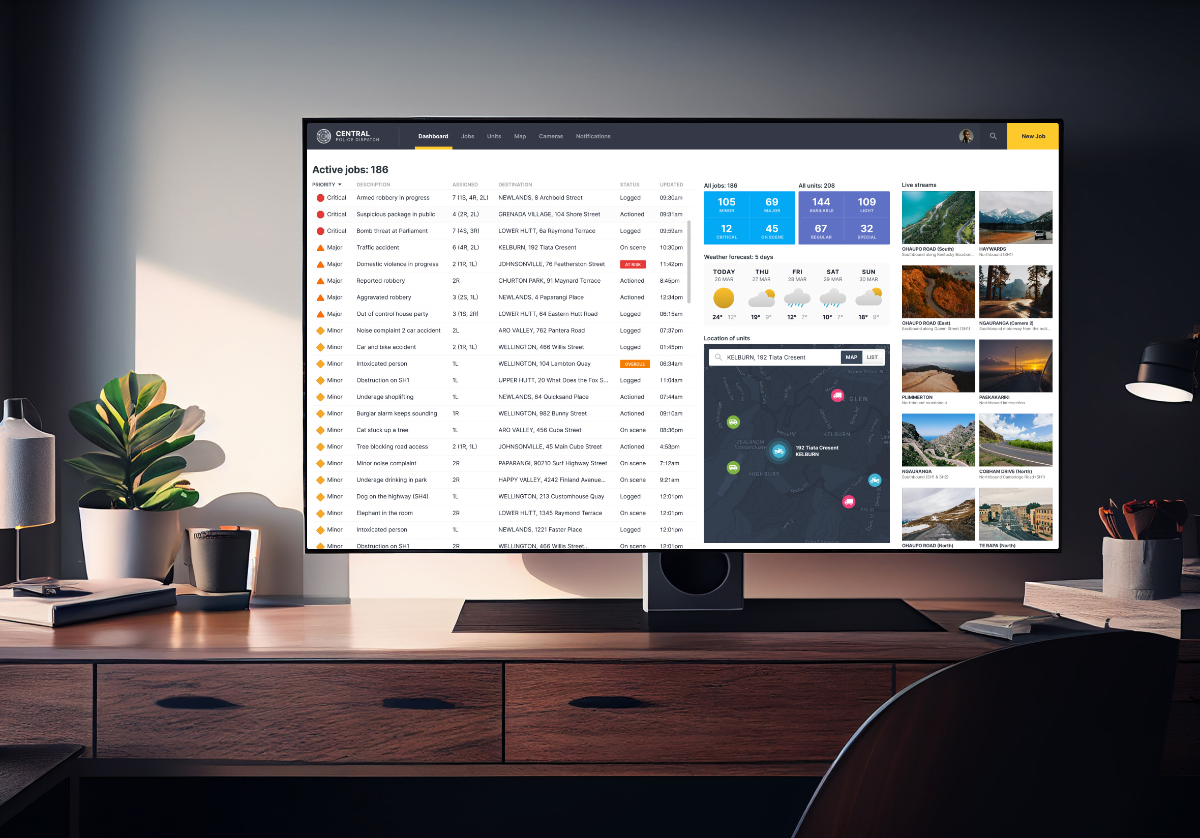 Large desktop monitor on a wooden desk displaying a Central Police Dispatch dashboard UI with active job feeds, unit metrics, map tracking, and live camera streams.