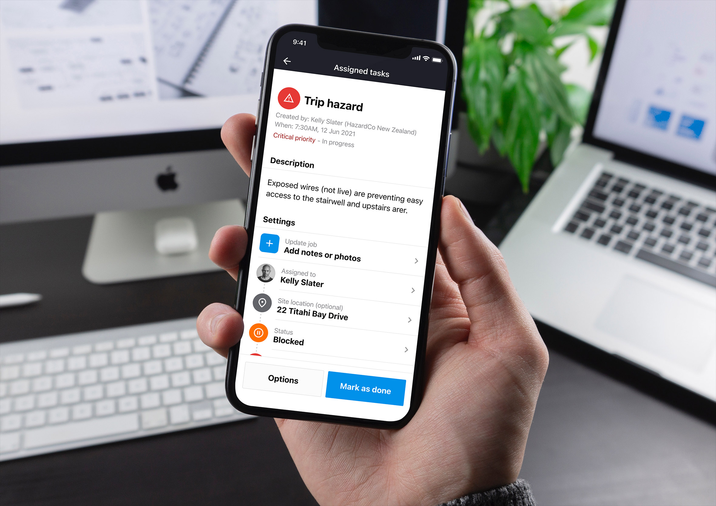 Hand holding an iPhone displaying a task detail page for a critical trip hazard report.