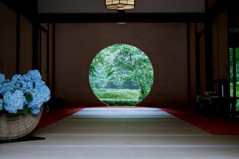 Symmetrical view of a serene Japanese tatami room with a large circular window framing lush green garden trees, illustrating minimalist spatial design and calm visual focus.
