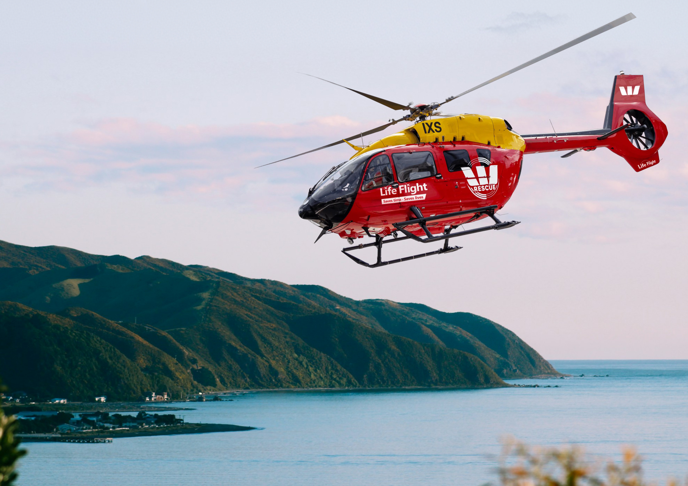 Action photograph of the red and yellow Life Flight Westpac Rescue Helicopter flying over the Wellington coastline, highlighting local emergency services and ocean safety.