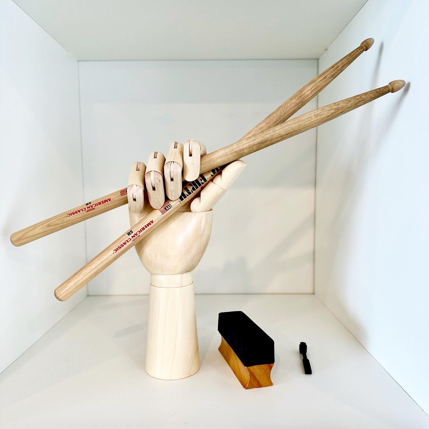 Wooden mannequin hand holding a pair of drumsticks on a shelf