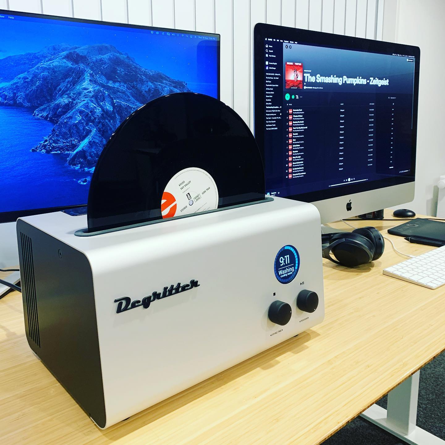 Degritter ultrasonic vinyl record cleaner on a desk beside a dual-monitor setup