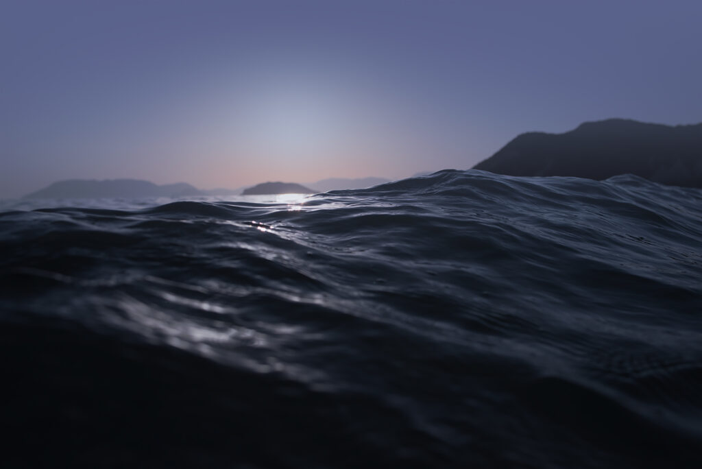 Dark ocean water swelling in the foreground with sunlight reflecting on the ripples, set against distant hilly islands under a twilight sky.