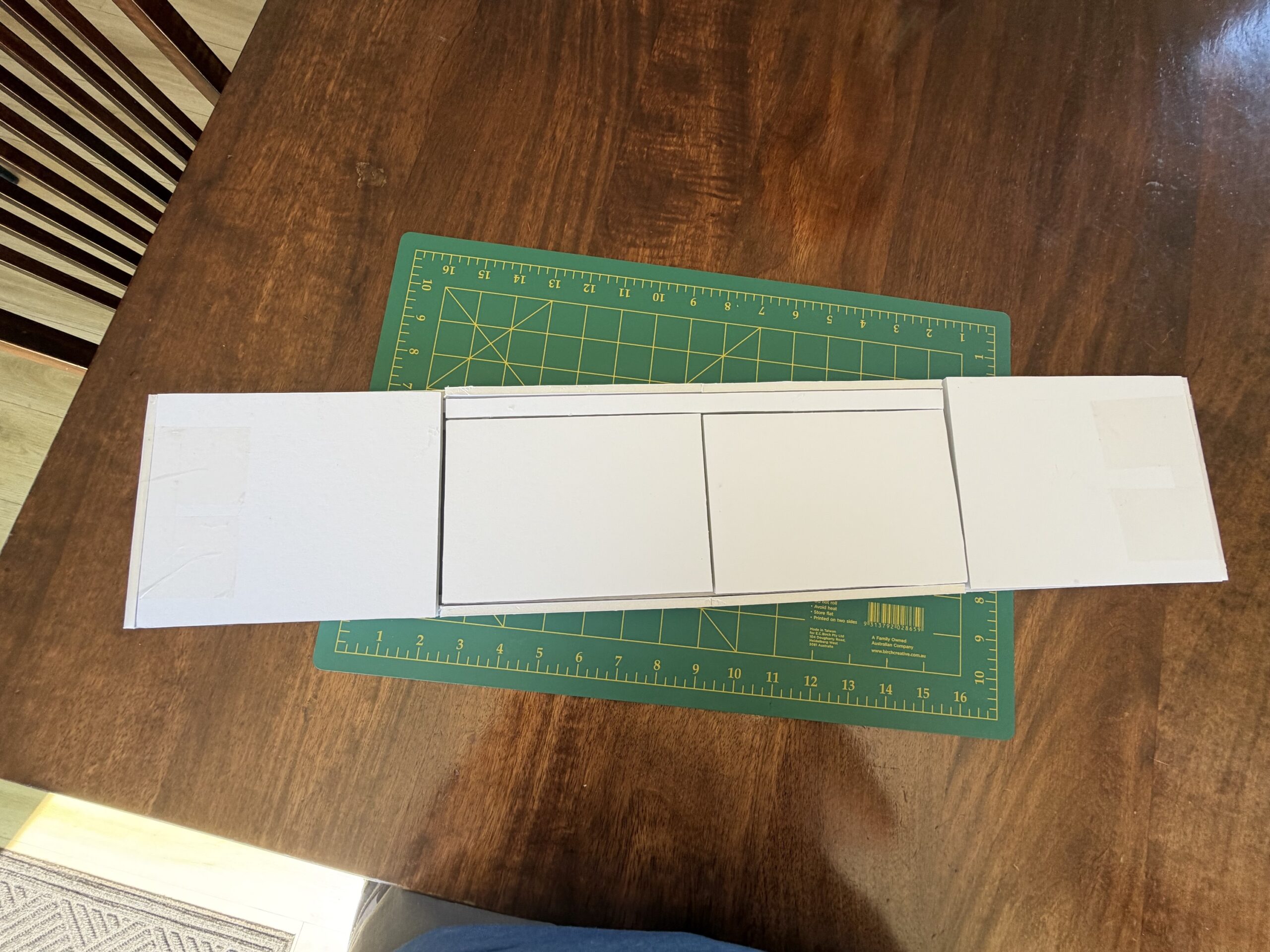 Top-down view of a scale foam-core prototype for custom Hi-Fi furniture with top sliding panels fully closed, resting on a green Birch cutting mat over a wooden table.