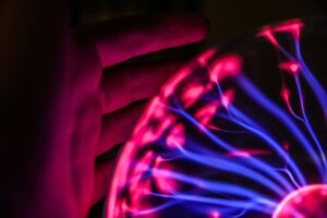 Close-up of a silhouette hand interacting with glowing pink and blue plasma ball energy streams, showcasing human curiosity and interactive physical-digital phenomena.