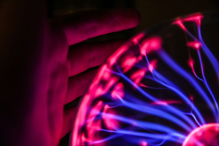 Close-up of a silhouette hand interacting with glowing pink and blue plasma ball energy streams, showcasing human curiosity and interactive physical-digital phenomena.