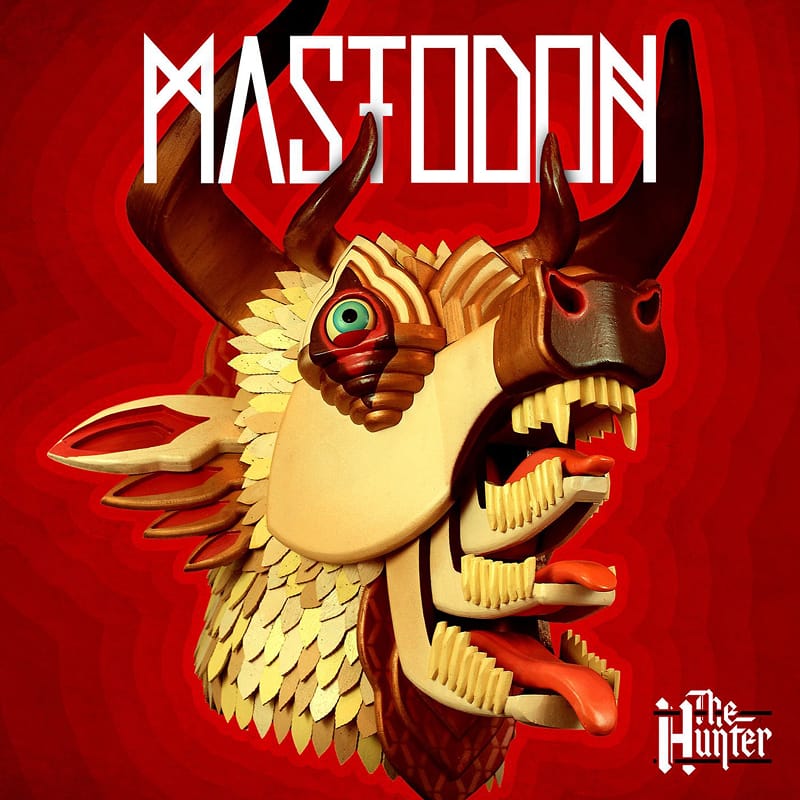 Wooden sculpture artwork for Mastodon's album The Hunter, showcasing a carved horned mask on a red background.