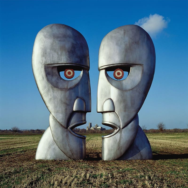Surreal landscape artwork for Pink Floyd's The Division Bell, featuring two giant metal head sculptures facing each other in a field.