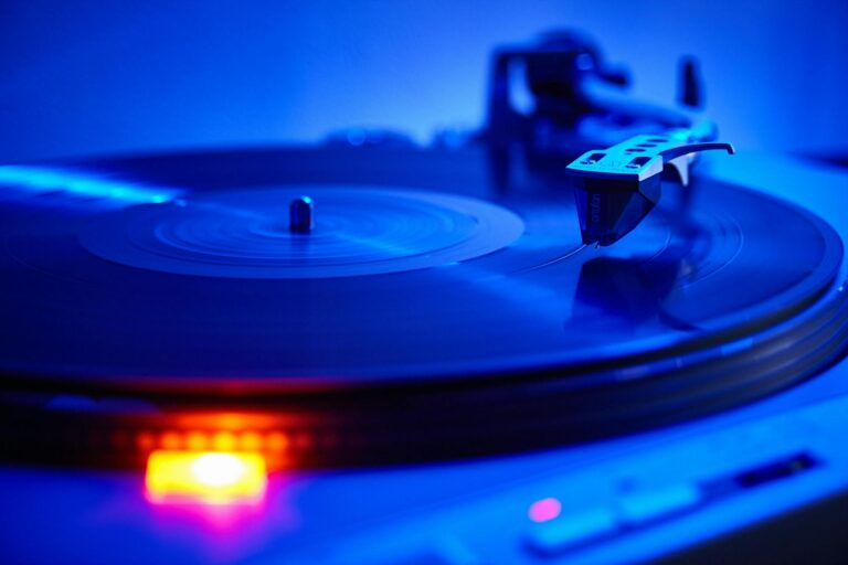 Macro shot of a turntable stylus tracking a spinning black vinyl record illuminated by neon blue lighting, capturing tactile analogue experiences and audio craft.