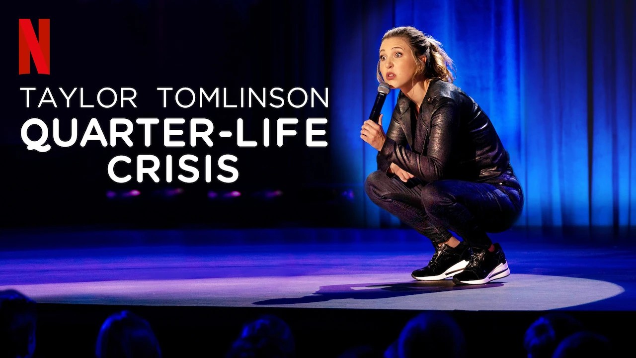 Promotional poster for Taylor Tomlinson's stand-up comedy special Quarter-Life Crisis showing Tomlinson squatting on stage holding a microphone.