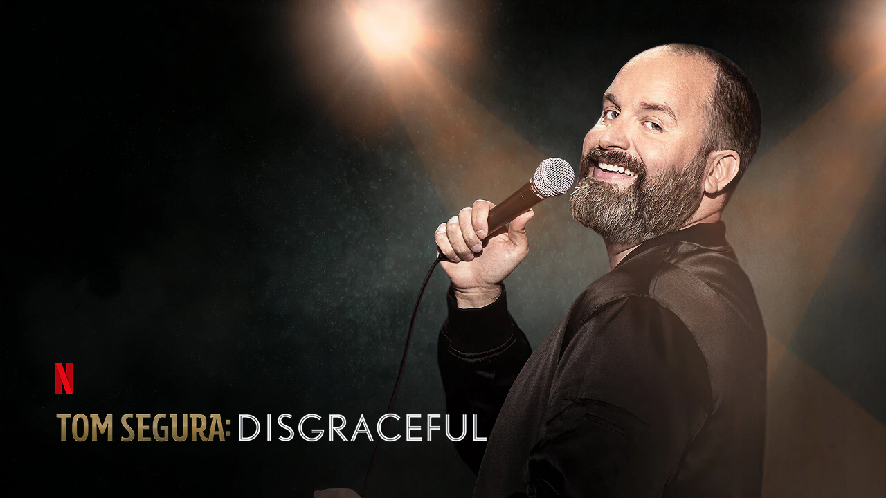 Promo image for Tom Segura's stand-up comedy special Disgraceful showing Segura illuminated under a spotlight with a microphone.