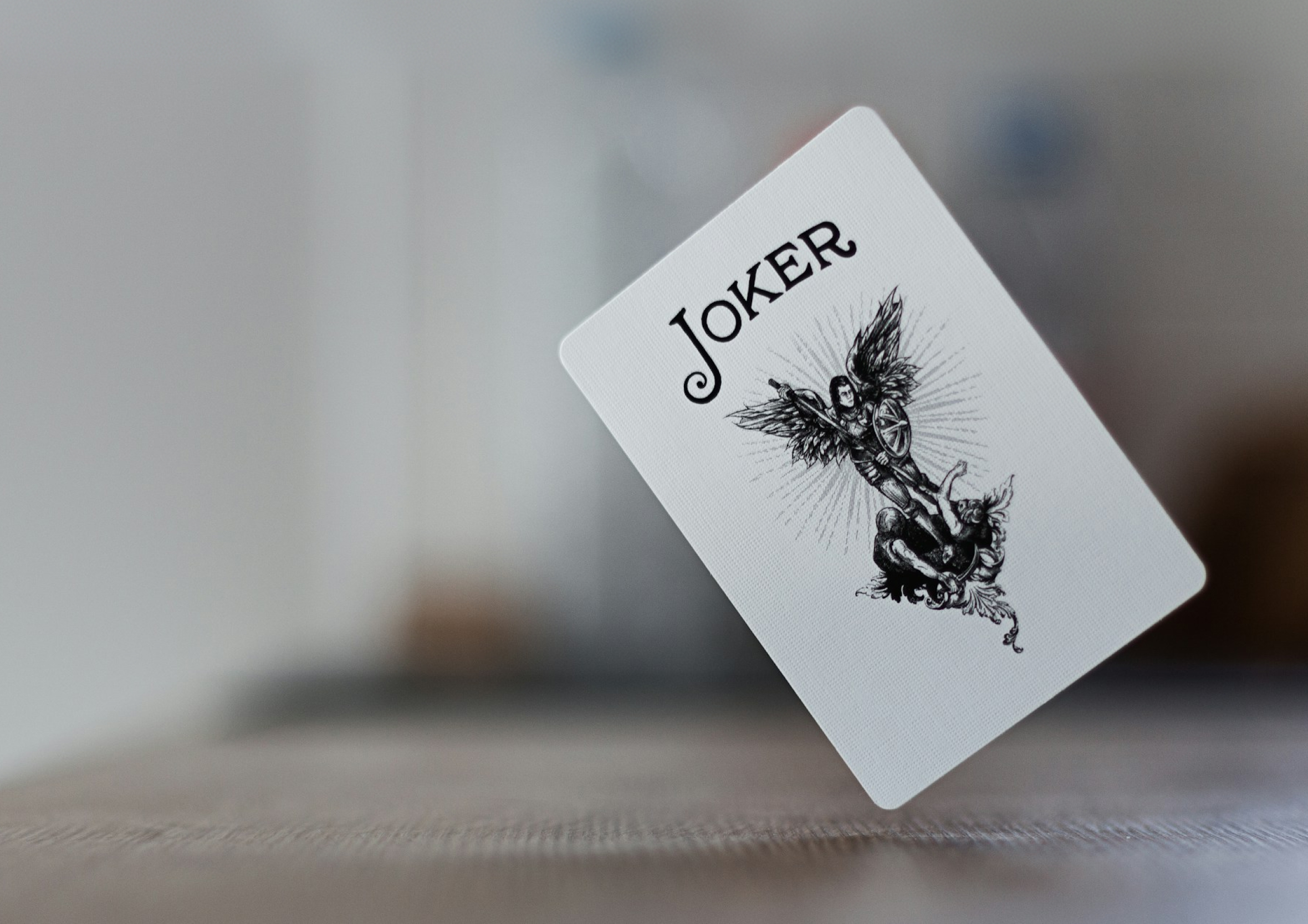 Macro photograph of a floating Joker playing card featuring an intricate black and white illustration of a winged warrior, capturing detailed line work for visual design inspiration.