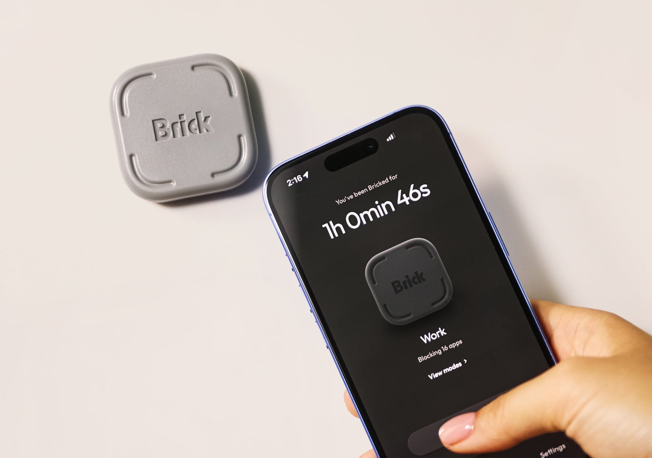 Hand holding a smartphone running the Brick app next to the physical Brick device