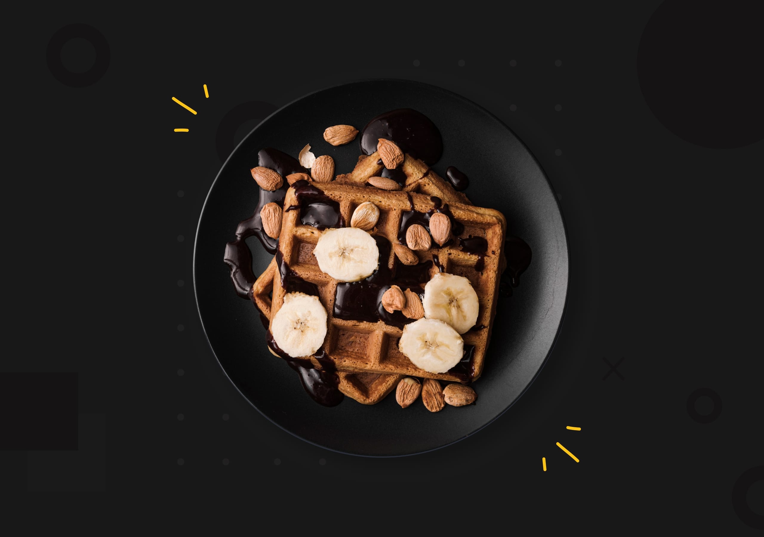 Top-down view of golden waffles on a dark plate topped with fresh strawberries, blueberries, sliced almonds, and maple syrup.