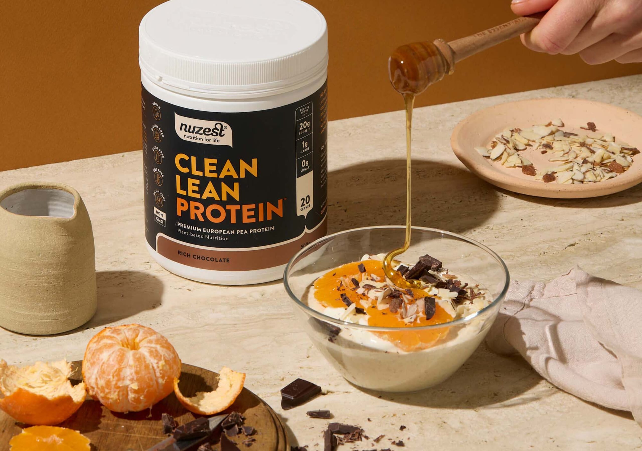 A tub of Nuzest Clean Lean Protein next to a breakfast bowl being drizzled with honey
