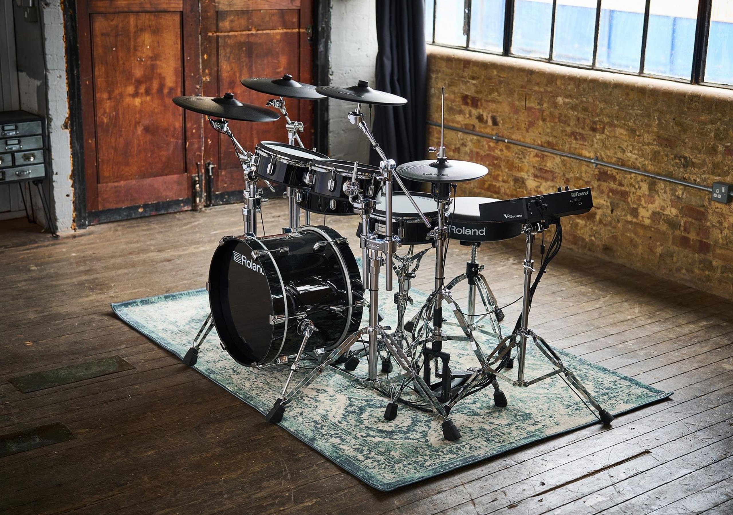 A Roland VAD507 electronic drum kit with chrome hardware, set up on a rug in an industrial loft space with brick walls.